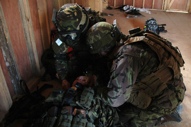 Afghánci (rumunští vojáci) a Češi společně poskytují první pomoc. Jejich kolegové mezitím přinášejí další zraněné